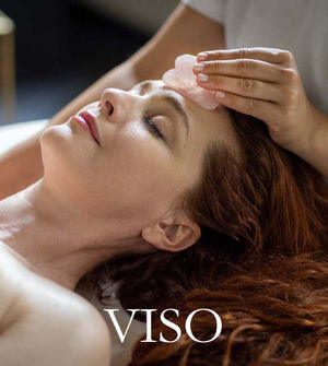 Modella sdraiata sul lettino mentre un’operatrice massaggia il viso con una pietra da massaggio.